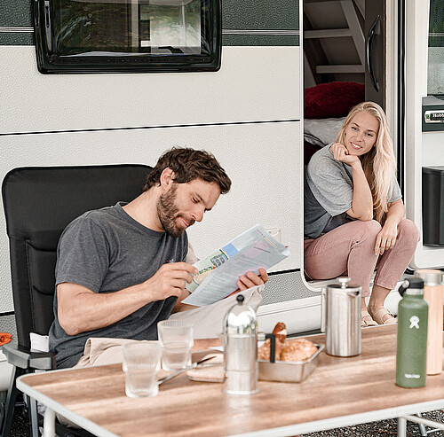 Mann plant Wanderung mit Wanderkarte im Campingurlaub und Frau sitzt daneben - Alpsee Camping Immenstadt