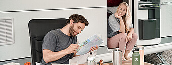 Mann plant Wanderung mit Wanderkarte im Campingurlaub und Frau sitzt daneben - Alpsee Camping Immenstadt