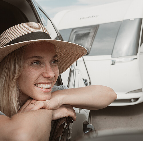 Lächelnde Frau mit Sonnenhut im Auto mit Wohnwagen - Alpsee Camping Immenstadt