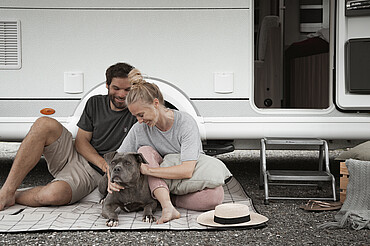 Paar streichelt Hund vor Wohnwagen - Alpsee Camping Immenstadt