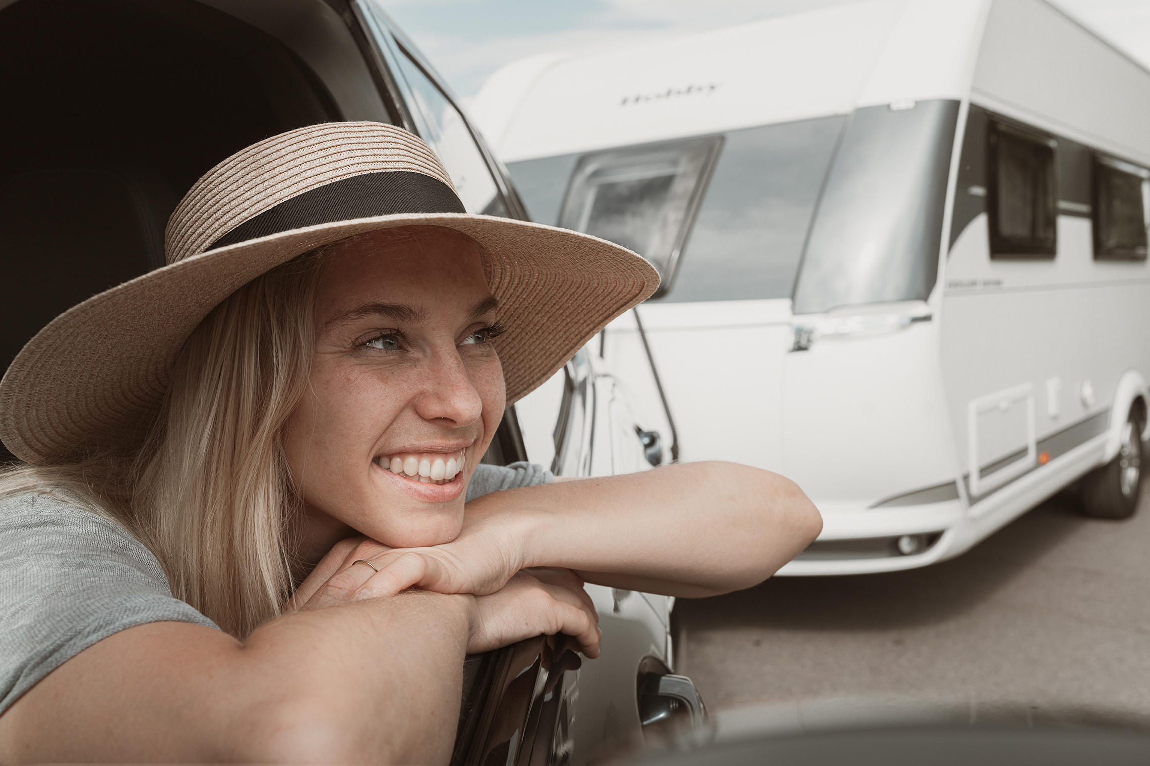 Lächelnde Frau mit Sonnenhut im Auto mit Wohnwagen - Alpsee Camping Immenstadt